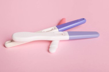 Evde hızlı hamilelik teşhisi. İzole edilmiş pembe pastel arka planda iki çubuklu hamilelik test kitleri. Uzayı kopyala. Kadın sağlığı, jinekoloji ve tıp konsepti. Doğum planlama konsepti