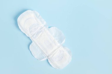 İzole edilmiş mavi arka planda, beyaz, emici, regl yastığının üst görüntüsü. Kadın sağlığı ve hijyen kavramı. Adet ve aylık döngü.
