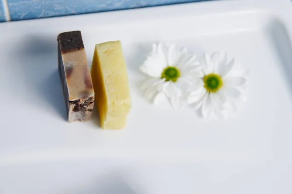 View from above of organic hand made soap bars with grape seeds and coffee beans, near chamomile flowers on wash basin. Natural eco-friendly cosmetics, home spa, body care, hygiene and beauty concept