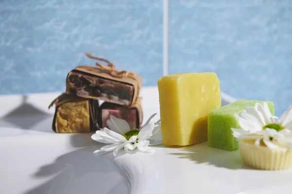 Still life. Assortment of craft organic soap bars with herbal ingredients and essential oils, for purity, home spa, skin and body care, on the bathroom wash basin against blue marble wall background