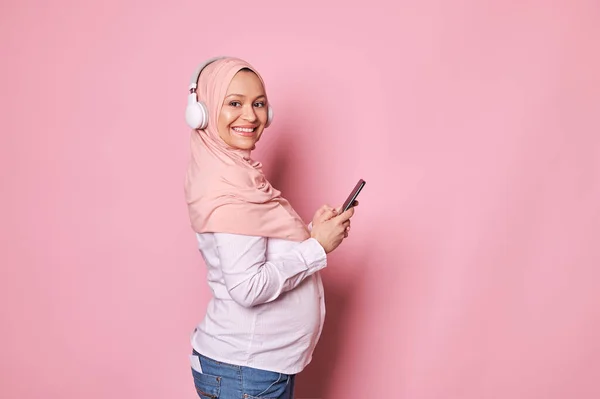 Щаслива Вагітна Мусульманка Рожевому Хіджабі Навушниках Перевіряє Нове Мобільне Застосування — стокове фото