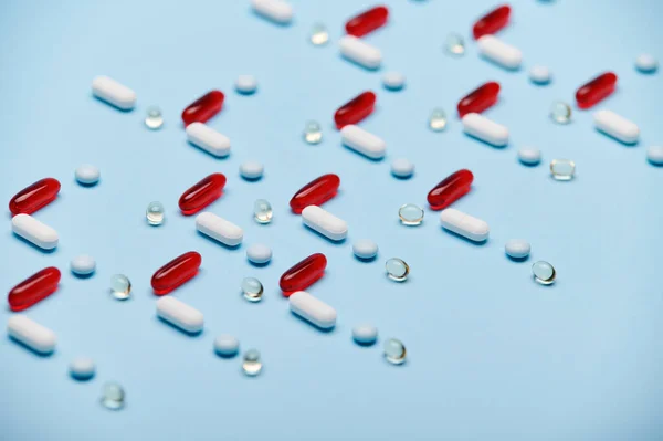 Medical background with red gelatin translucent capsules with essential oils, Omega 3 or fat-soluble vitamins and pharmaceutical pills laid out in pattern on blue surface. Pharma industry and business
