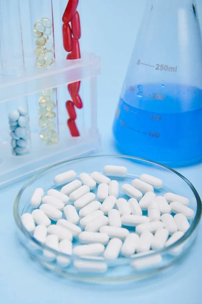 World Health Day. Pharmaceutical industry. Pharma business. Clinical research concept. Therapeutic medical pills in petri dish, fluid solution in lab flask and gel capsules in test tube, blue backdrop