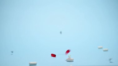 Farklı ilaç ve kapsüllerle 4K Çözünürlük görüntüleri mavi arka plana dökülüyor. İlaç endüstrisi bir ilaç sektörü konseptidir. Ağır çekim. Uzayı kopyala Model