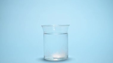 Hastalar coşkulu tableti bir bardak suya koyuyorlar. İzole edilmiş mavi arka planda köpüklü hapların eridiğini görüyoruz. Reçeteli ilaçlar. Ağrı kesici antipiretik. İlaç endüstrisi