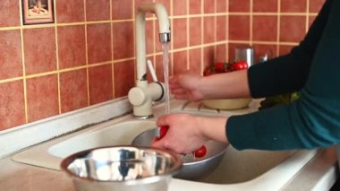 Mutfak lavabosunda taze olgun organik domatesleri akarsu altında yıkayan kadınların yakın çekim videosu. Tanınmayan hizmetçi evdeki rahat mutfakta salata pişirmek için sebze yıkıyor. 4K Çözünürlüğü