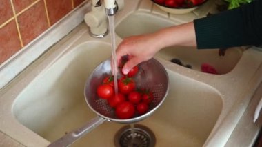 Ev mutfağında sağlıklı çiğ vegan salatası pişirmek için lavaboda domates yıkayan tanınmamış bir ev kadınının yukarıdan görünüşü. Sağlıklı beslenme. Diyet olsun. Vejetaryenlik ve sağlıklı yaşam tarzı kavramı. 4K