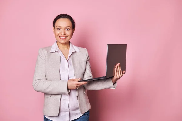 Mature Latin American business woman, entrepreneur smiling, confidently looking at camera, holding laptop, isolated on pink background. People, career, business, startup, job and recruitment concept
