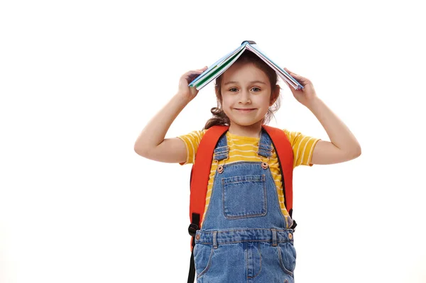 白种人聪明的学生小女孩 正面愉快的一年级生 头顶着翻开的书本 带着可爱的笑容看着相机 与白色背景隔离 回学校去教育概念 — 图库照片