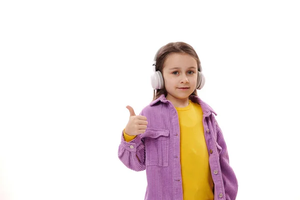 ワイヤレスヘッドフォンで素敵な白人の5 6歳の少女は Okサインを示し 合意と肯定的な感情を表現し 白い背景に隔離されたカメラを見て笑顔 広告スペースのコピー — ストック写真