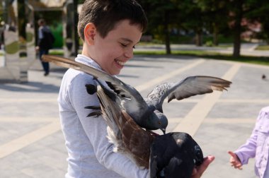 Yakışıklı, neşeli bir çocuğun portresi gülümseyen, uçan güvercin sürüsünü besleyerek eğlenen yaz parkında. Mutlu tasasız çocukluk kavramı ve doğa ve hayvanlara sevgi aşılamak.