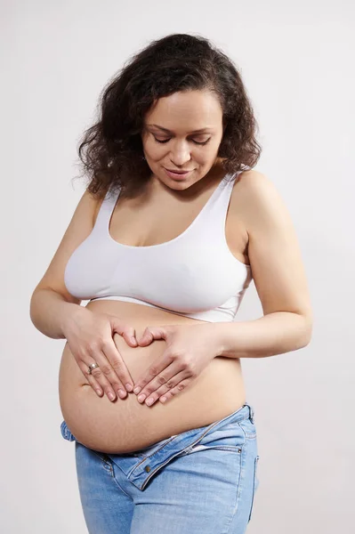 穿着白色内裤和牛仔的年轻孕妇 双手放在肚子上 与白色背景隔离 漂亮的肉质女性怀孕了 怀孕24周 — 图库照片
