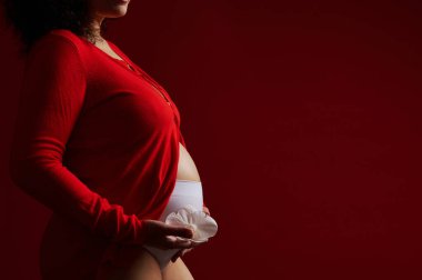 Hamile bir kadının yakın plan portresi, hamile bir anne, izole edilmiş kırmızı arka planda beyaz bir çiçek ile çıplak karnına poz veriyor. Kadın Sağlığı. Sağlıklı olmak. Hamilelik. Doğumhane. Jinekoloji