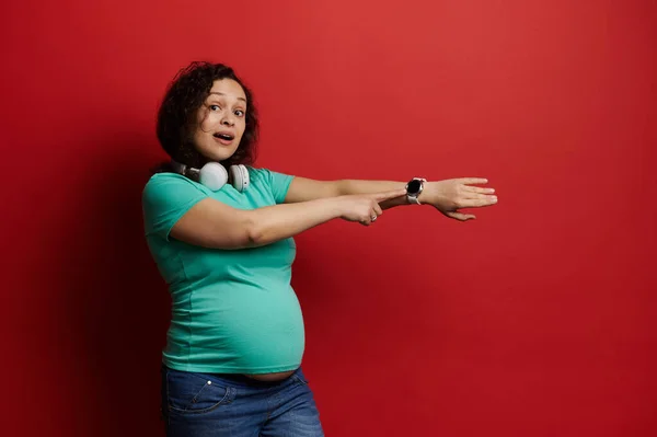 Krásná Těhotná Žena Bezdrátovými Sluchátky Ukazující Kameru Její Chytré Náramkové — Stock fotografie