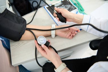 Hamile bir kadının tansiyonunu ölçmek için tonometre kullanan bir jinekolog hemşirenin yakın plan görüntüsü. Hamilelik öncesi hipertansiyon ve eklampsinin erken teşhisini önlemek için.