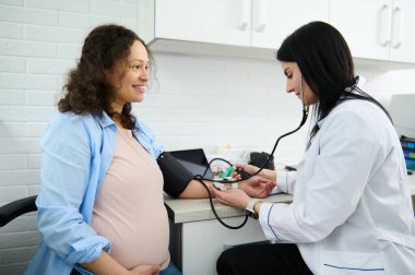 Kadın doğum uzmanı jinekolog doktor hastanedeki hamile kadının kan basıncını ölçüyor. Hamilelik kaynaklı hipertansiyon ve eklampsi ve preeklampsi konsepti. Jinekoloji