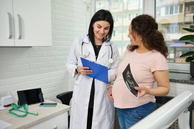 Gülümseyen olgun hamile kadın, jinekoloji kliniğindeki jinekolog kadın doğum uzmanını düzenli sağlık kontrolünde ziyaret ediyor. Hamilelik ve hamilelik kavramı. Sağlık ve ilaç servisi. Ultrasonografi