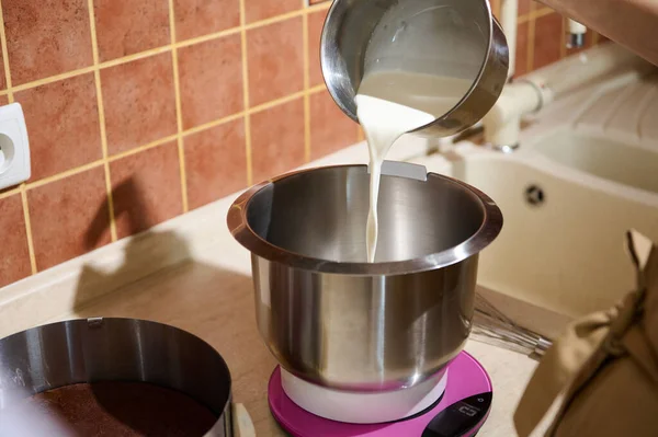 stock image Close-up process of pouring fresh cream into stainless steel bowl of food processor with planetary mixer, for preparing whipped cream for chocolate cake at home kitchen. Cooking triple chocolate cake