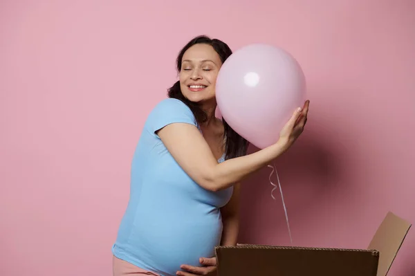 stock image Delightful conscious pregnant woman gently hugging a pink balloon, feeling happy positive emotions expecting a baby girl, enjoying her pregnancy, isolated over pink background. Gender reveal party