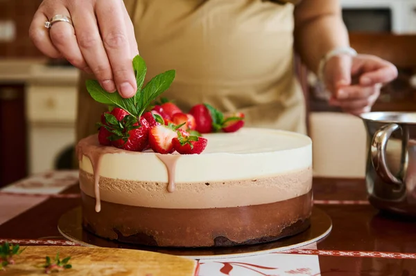 stock image Close-up pastry chef putting mint leaves and fresh strawberries on top of homemade triple chocolate cake - a layered mousse dessert, made with whipped cream and melted confectionery belgian chocolate