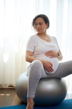 Güzel Afro-Amerikan hamile kadının dikey portresi karnını tutuyor, evde doğum öncesi esneme egzersizlerinden sonra rahatlıyor. Aktif ve sağlıklı yaşam tarzı kavramı