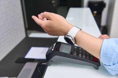 NFC teknolojisiyle faturayı akıllı saatle ödeyen bir kadının yakın çekimi. Müşteri, ukalalık yaparak temas kurmadan ödeme yapıyor. Saha iletişimine yakın. - İnsanlar. Müşteri hizmetleri. Kablosuz teknolojiler