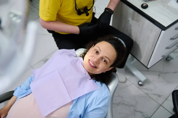 多种族的年轻孕妇在牙科诊所接受牙科诊所检查时的肖像 她期待着孩子 坐在牙椅上 脸上带着美丽的笑容 看着相机 从上面看 — 图库照片