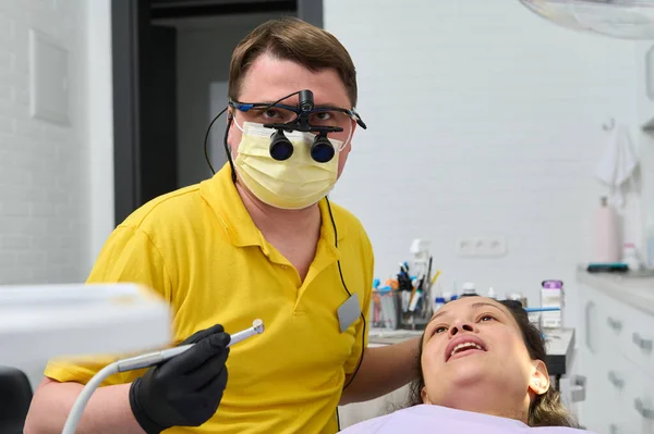 Profesjonalny Dentysta Noszący Ochronną Maskę Medyczną Lornetkę Ortodonty Trzyma Wiertarkę — Zdjęcie stockowe
