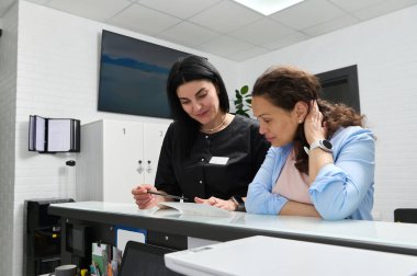 Beyaz, kendine güvenen kadın dişçi danışmanı hasta, hamile bir kadın hamilelik sırasında dişçi kliniğinde yapılması gereken diş tedavisi hakkında, resepsiyonda duruyor.