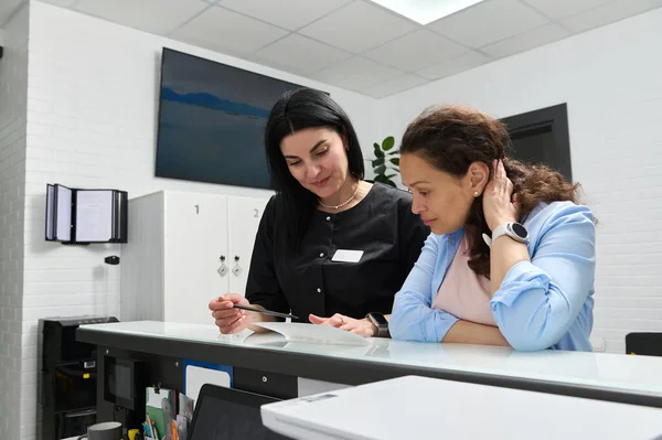 Beyaz, kendine güvenen kadın dişçi danışmanı hasta, hamile bir kadın hamilelik sırasında dişçi kliniğinde yapılması gereken diş tedavisi hakkında, resepsiyonda duruyor.