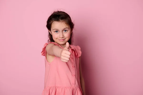 広告スタジオポートレートの白人可愛い女の子5 スタイリッシュなピンクのドレスで 親指アップ カメラを見て肯定的な感情を表現します ピンクの背景に孤立 — ストック写真