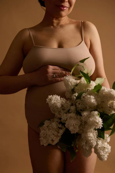 Środek Ciężarnej Kobiety Trzymającej Bukiet Białego Liliowego Pozującego Beżowym Tle — Zdjęcie stockowe