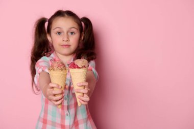 Tatlı bir kızın ellerinde leziz dondurmalarla waffle külahlarının ayrıntıları. Elinde kamera, dondurulmuş tatlıyı taze tutuyor. Pembe arka planda izole edilmiş ve reklam alanı olan. Yaz konsepti