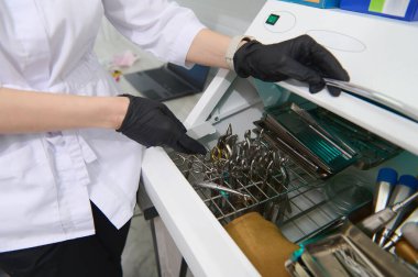 Yakın plan dişçiler siyah eldiven giyer, ultraviyole otoklav sterilizatörünü açar, steril diş aletleriyle sterilize makinesini çalıştırır. UV termostatı. Sterilizasyon. Ultraviyole lambalı dezenfeksiyon. Dişçilik