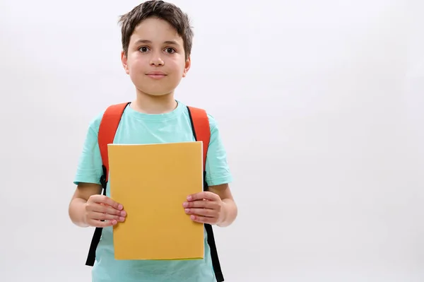 一个白种人少年的有自信的画像 一个11岁至13岁的快乐的 英俊的学童 背着背包 拿着练习本 带着可爱的微笑看着相机 在白色的工作室背景下与世隔绝 — 图库照片