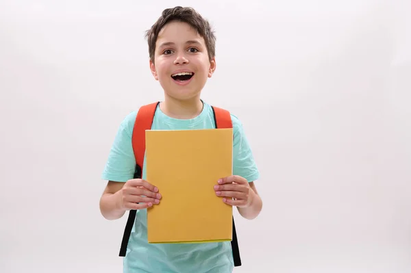 白人の感情的な幸せな十代の少年は 白い孤立した背景の上に立って カメラを見て笑顔の教科書を保持しています 広告スペースをコピーします 新学期の学校に戻る — ストック写真