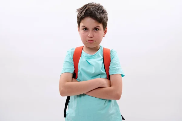 Portrait of a sad, distressed, offended preteen boy, tearful school kid with arms folded, feeling sadness after act of bullying at school, looking at camera, isolated on white studio background