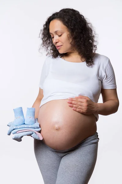 美丽的准妈妈 多民族的成年快乐孕妇 抱着新生儿的衣服 摆出赤裸的肚子 与白色的工作室背景隔离 怀孕了母性 怀上孩子 — 图库照片