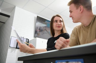 Sağlıklı bakım ve ilaç kavramı. Güzel hemşire kadın, hasta yakışıklı adamla tartışıyor. Modern klinikteki resepsiyonda ya da ayakta tedavi gören adamla konuşuyorlar.