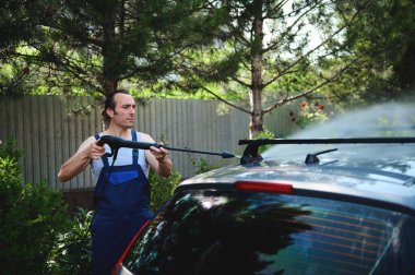 Yakışıklı kaslı beyaz adam ya da araba tamircisi dışarıda bir aracı yıkıyor, yüksek basınçlı su temizleyiciyi arabanın çatısına sıkarken görüldüğü gibi yönlendiriyor. Otomobil hizmeti kavramı