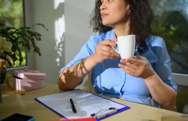 Seçici odaklanma. Orta yaşlı bir iş kadını, girişimci, çiçekçi, elinde beyaz bir fincan kahve olan bir dekoratörün elinde dosyayla oturmuş çiçekçiden emirler alan...