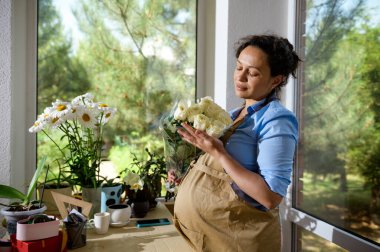 Çok etnik, kıvırcık, güzel, enfes hamile bir kadın. Hamileliği boyunca çiçek tasarım stüdyosunda çalışan çiçekçi girişimciye ilham verdi. Festival için elinde bir buket taze gül tutuyor.