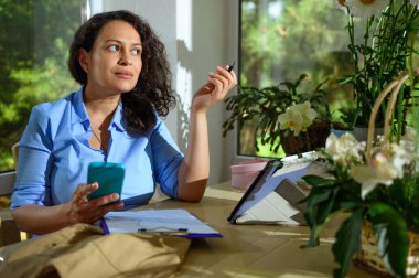 Düşünceli, çok ırklı kadın girişimci, cep telefonu kullanıyor, panoya resim çiziyor, çiçek tasarım stüdyosundan özel şenlik için sipariş alıyor. - İnsanlar. İş için. Ayarlamalar ve hediyeler