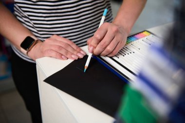 Mavi renkli kalemi test eden, siyah bir kağıt üzerine çizen kadının el görüntüsü. Okul kırtasiyesi. Malzeme çiziyorum. Yaratıcı sanat mağazası. Ofis malzemeleri dükkanı. - İnsanlar. Hobiler. - Sanat. Yaratıcılık