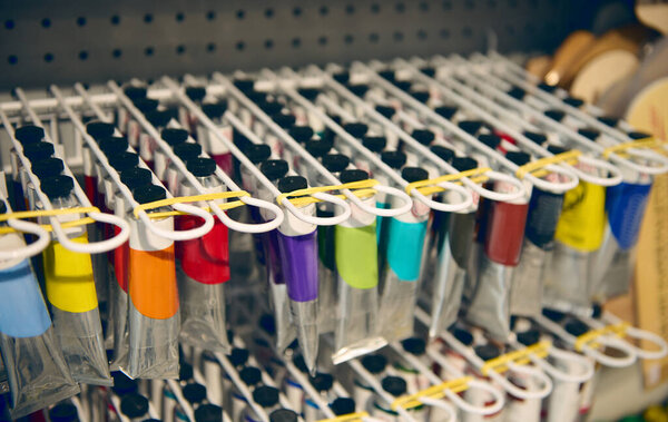 Акриловые, акварельные или масляные краски в лакокрасочных трубах, висящих на полках, выставлены на продажу в художественном магазине. Школьный магазин канцелярских товаров. Супермаркет канцтоваров. Концепция изобразительного искусства и творчества. Натюрморт