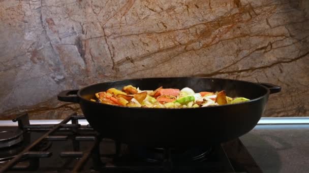 近くのシェフが鋳鉄製のフライパンで刻んだ野菜を攪拌します 季節の野菜から野菜のシチューを調理するフライパンで台所のストーブの上に 料理だ フランスのラタトゥイユ ラグーの準備 — ストック動画