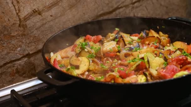 近くのシェフが鋳鉄製のフライパンで刻んだ野菜を攪拌します 季節の野菜から野菜のシチューを調理するフライパンで台所のストーブの上に 料理だ フランスのラタトゥイユ ラグーの準備 — ストック動画