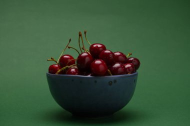 Koyu yeşil arka planda izole edilmiş, olgun organik kirazlarla dolu mavi bir seramik kaseyle sakin bir hayat. Yemek arkaplanı. Sağlıklı beslenme. Yaz hasadı. Meyveler ve meyveler