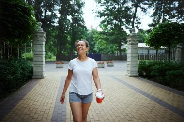 Beyaz tişörtlü ve günlük kot şortlu mutlu, kendinden emin genç kadınlar sokakta yürürken başka tarafa bakıyor. Güzel, sıcak bir yaz gününde parkta yürüyen kadın turist.