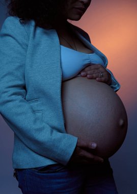 Güzel hamile bir kadının göbeğinin fütüristik çekimlerini yakın plan çekiyoruz. Müstakbel anne, büyük karnını okşuyor. Neon ışıklı arka planda izole edilmiş. Bir bebek bekliyorum. Çocuk doğurmak. Hamilelik